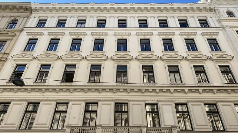 Klassische Fassade eines Altbaus mit vielen Fenstern und dekorativen Elementen unter blauem Himmel.