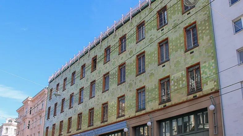 Historisches Gebäude mit markanter grüner Fliesenfassade und vielen Fenstern in der Stadt.