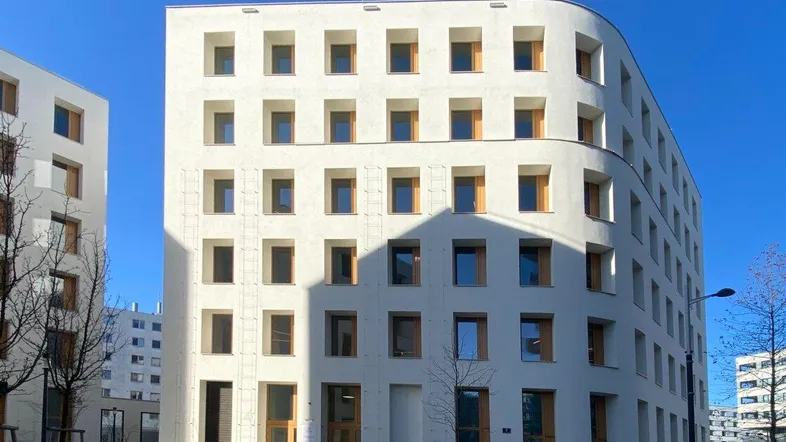 Modernes, weißes Gebäude mit vielen Fenstern und abgerundeter Ecke unter blauem Himmel.