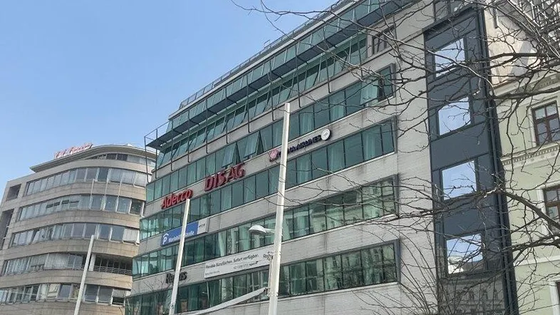 Moderne Bürogebäude-Fassade mit großen Fenstern und Geschäften im Erdgeschoss an einer belebten Straße.
