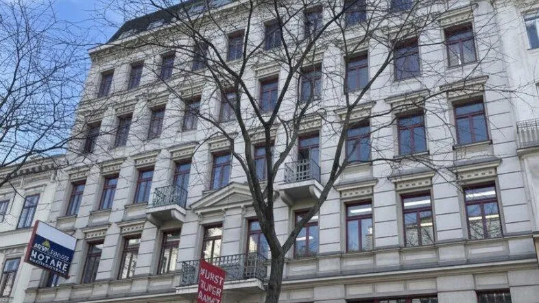 Klassische Fassade eines mehrstöckigen Gebäudes mit Geschäften im Erdgeschoss und Wohnungen darüber, an einem klaren Tag.