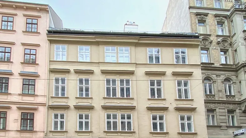 Historische Fassade eines Mehrfamilienhauses in der Stadt mit vielen Fenstern und Geschäften im Erdgeschoss.