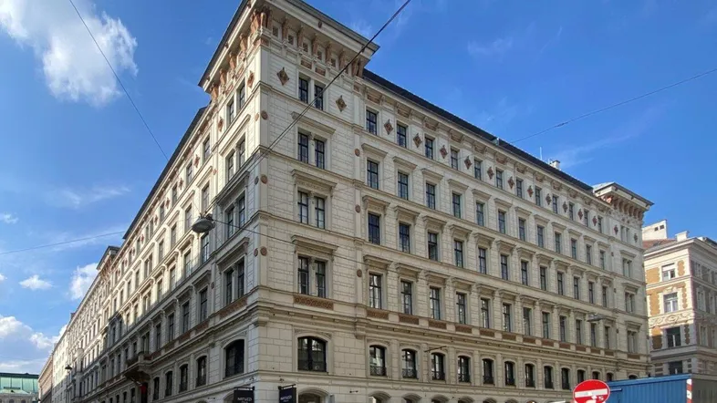 Historisches Gebäude mit klassischer Fassade und vielen Fenstern an einer städtischen Straße unter blauem Himmel.