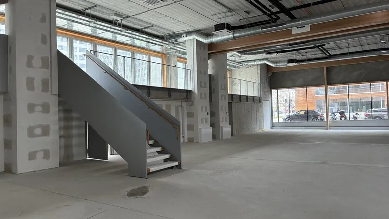 Geräumiger, unfertiger Gewerberaum mit hohen Decken, großen Fenstern und sichtbaren Installationen.