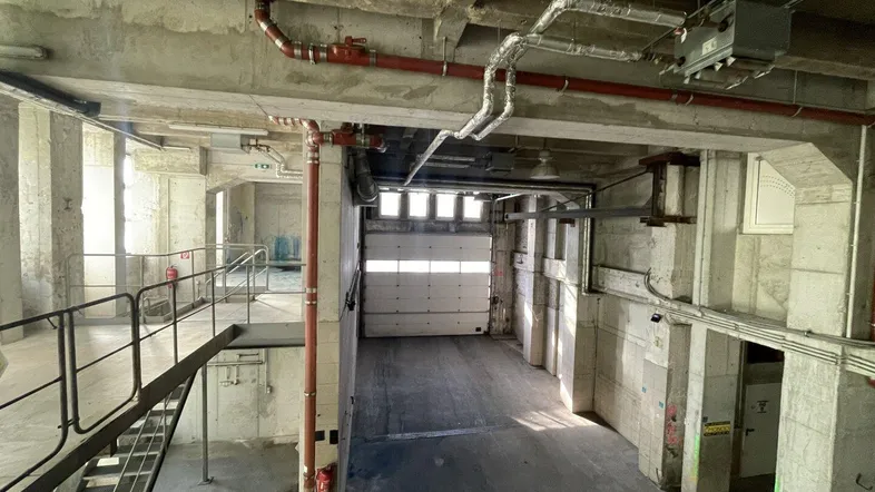Geräumiger Industrieraum mit Betonstrukturen, einer Treppe und einem großen Rolltor im Hintergrund.