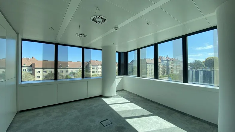 Heller Büroraum mit großen Fenstern, die viel Tageslicht hereinlassen und einen Blick auf die Stadt bieten.