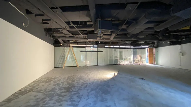 Leerer Gewerberaum mit hohen Decken, freiliegenden Installationen und großen Fensterfronten.