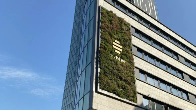 Modernes Hochhaus mit Glasfassade und vertikaler Begrünung unter blauem Himmel.