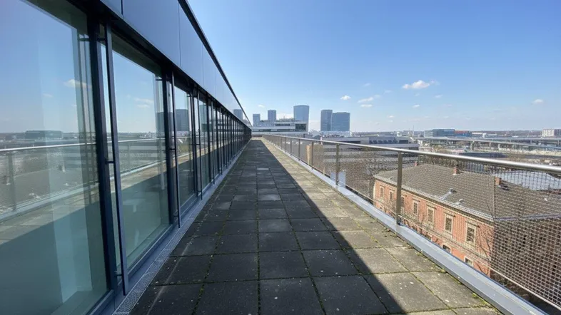 Lange Dachterrasse mit modernen Glasfassaden und weitem Blick auf die Stadt unter blauem Himmel.