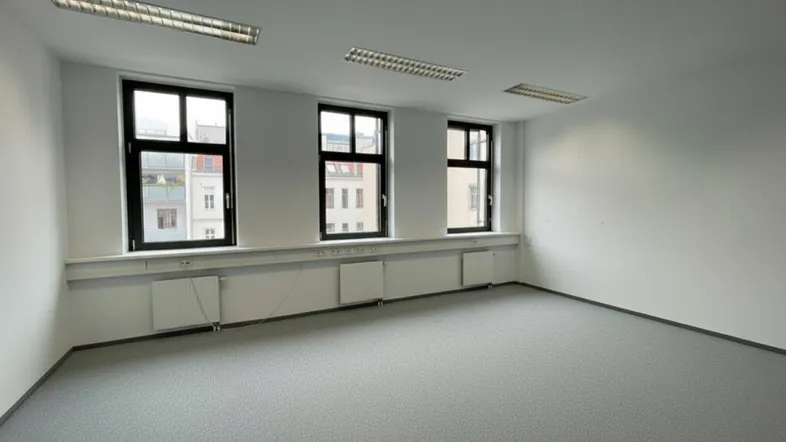 Geräumiges, leeres Büro mit drei Fenstern, weißen Wänden und grauem Teppichboden für flexible Nutzung.