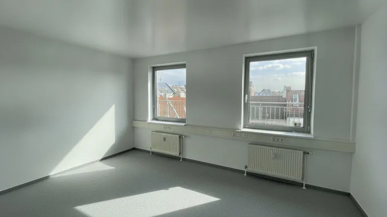 Leerer Büroraum mit zwei Fenstern, die Tageslicht hereinlassen und einen Blick nach draußen bieten.