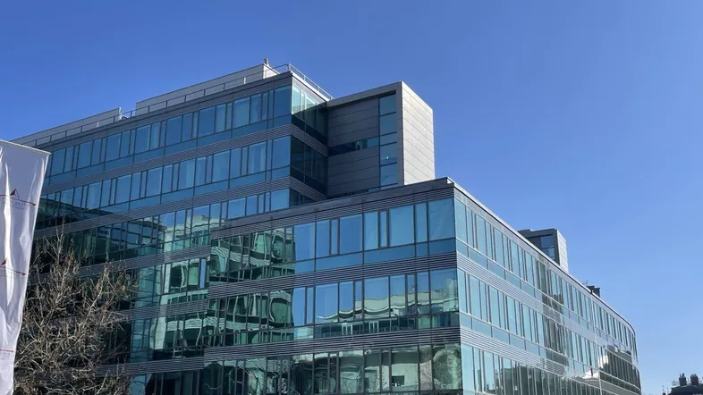 Modernes Bürogebäude mit großer Glasfassade unter strahlend blauem Himmel, das viel natürliches Licht verspricht.