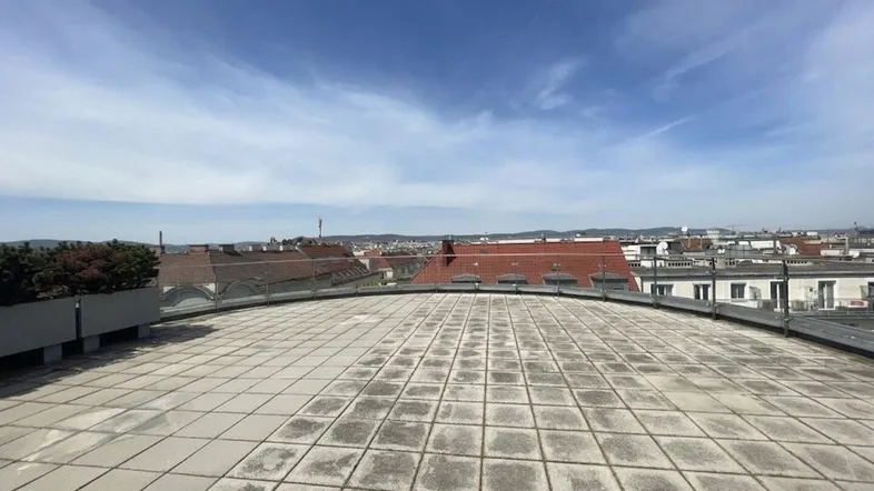 Weitläufige Dachterrasse mit Fliesenboden, Glasgeländer und Panoramablick über die Stadt.