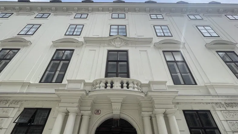 Eindrucksvolle weiße Fassade eines historischen Gebäudes mit vielen Fenstern und einem verzierten Eingangsbereich.