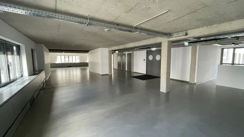 Großer, offener Büroraum mit Sichtbetondecke, Industriedesign und viel Tageslicht.
