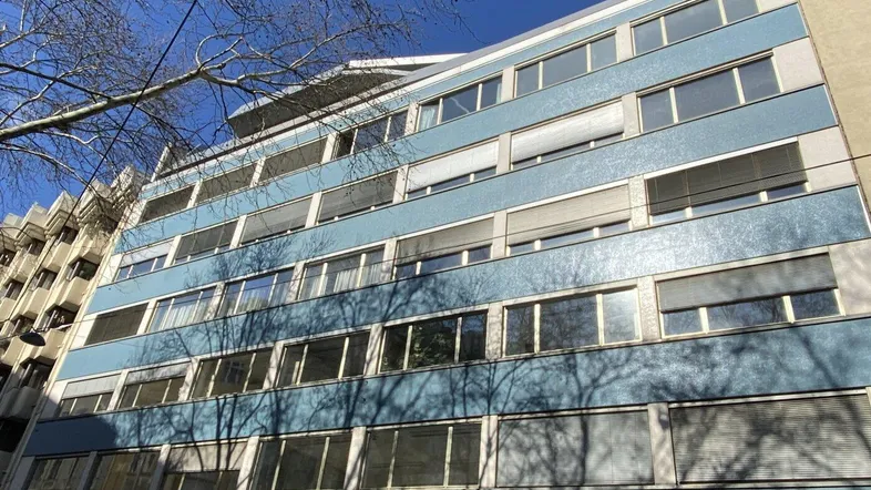 Mehrstöckiges Gebäude mit blauer Fassade und vielen Fenstern unter klarem blauem Himmel.