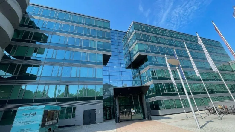 Modernes Bürogebäude mit beeindruckender Glasfassade und großzügigem Eingangsbereich unter blauem Himmel.