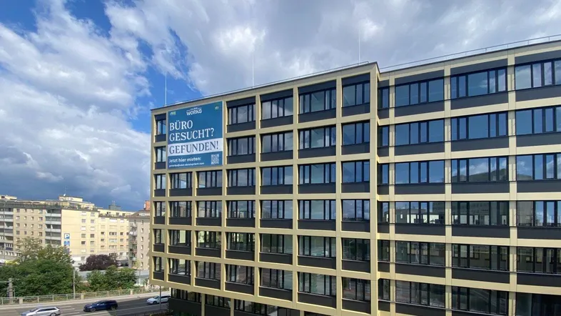 Modernes Bürogebäude mit vielen Fenstern und einer Werbetafel an der Fassade unter blauem Himmel.