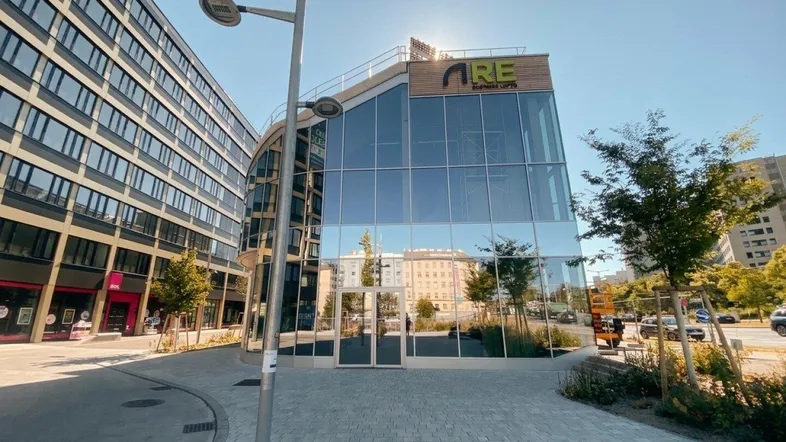 Modernes Geschäftsgebäude mit Glasfassade und gepflastertem Vorplatz unter strahlendem Sonnenschein.