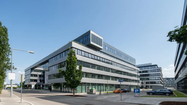 Modernes Bürogebäude mit Glasfassade und mehreren Etagen, umgeben von einer Straße und Parkplätzen.