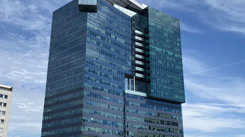 Modernes Hochhaus mit blauer Glasfassade und markanter Architektur unter blauem Himmel.