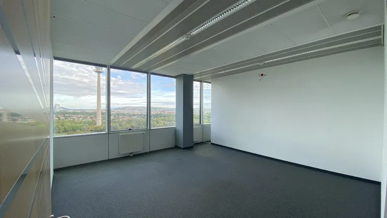 Geräumiges Büro mit Teppichboden und großen Fenstern, die einen weiten Blick über die Stadt bieten.