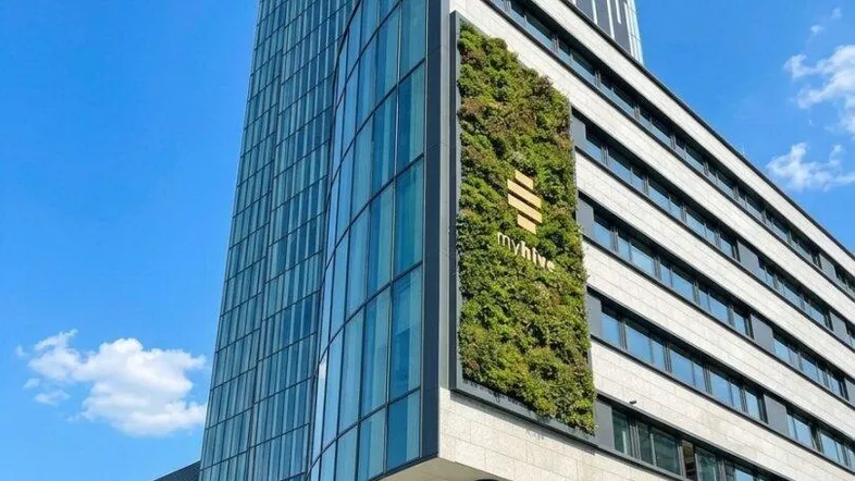 Modernes Hochhaus mit Glasfassade und vertikalem Garten, unter blauem Himmel.
