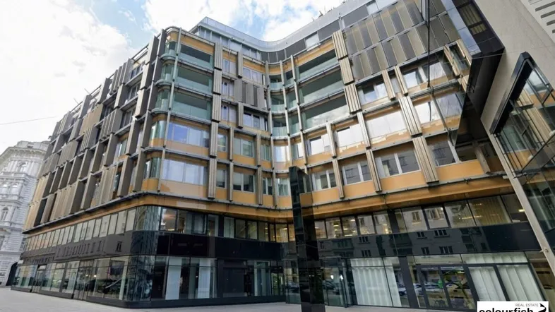 Moderne Bürogebäude-Fassade mit geschwungenen Linien und großen Glasflächen unter bewölktem Himmel.