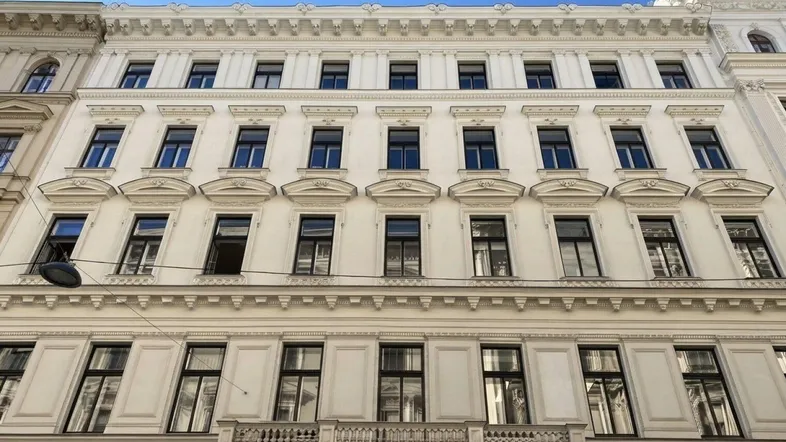 Klassische Fassade eines Altbaus mit vielen Fenstern und einem kleinen Balkon im Erdgeschoss.