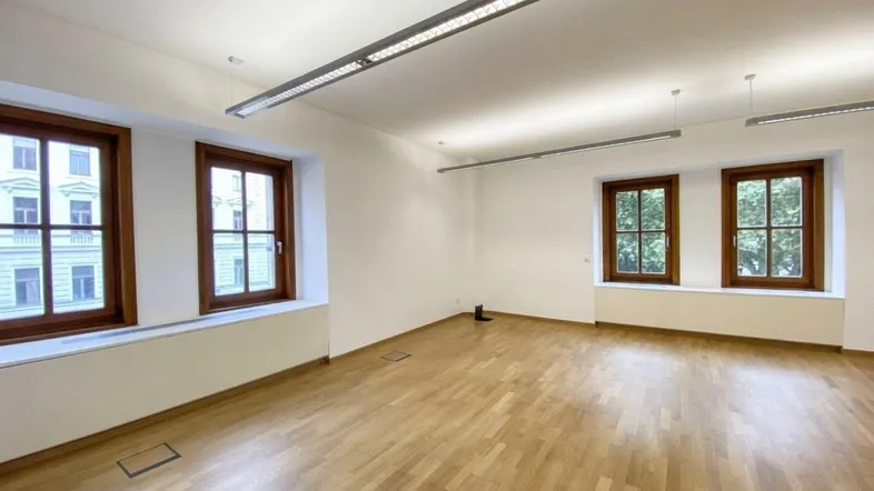 Geräumiges, helles Büro mit Holzboden und großen Fenstern, ideal für verschiedene Arbeitsbereiche.