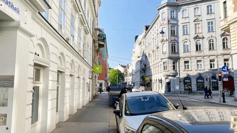 Blick auf eine belebte Straße mit historischen Gebäuden und geparkten Autos unter blauem Himmel.