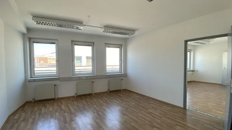 Heller Büroraum mit Holzparkettboden, großen Fenstern und Blick auf die Umgebung, ausgestattet mit Standardbeleuchtung.