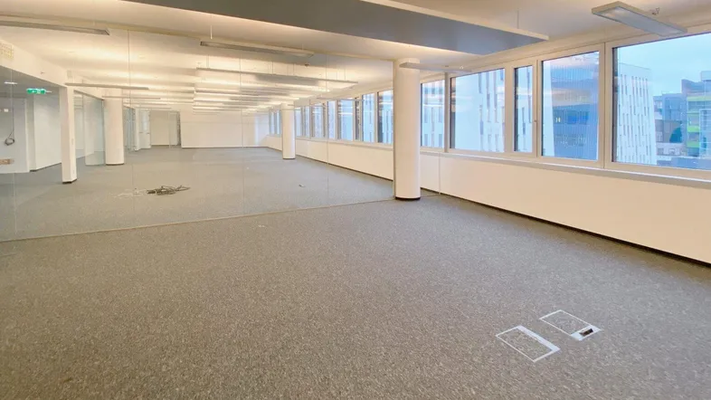Geräumiges, modernes Büro mit Teppichboden und großen Fenstern, die viel Tageslicht hereinlassen.
