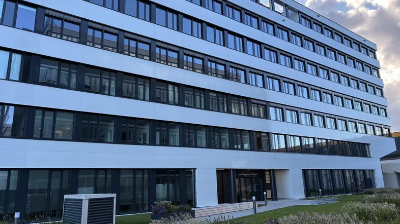 Modernes Bürogebäude mit weißer Fassade und vielen Fenstern, umgeben von gepflegten Grünflächen.