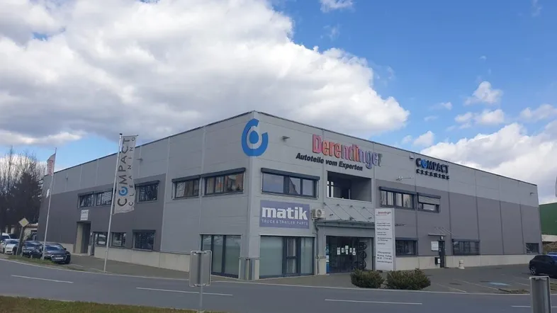 Modernes Gewerbegebäude mit grauer Fassade und blauen Akzenten unter bewölktem Himmel.