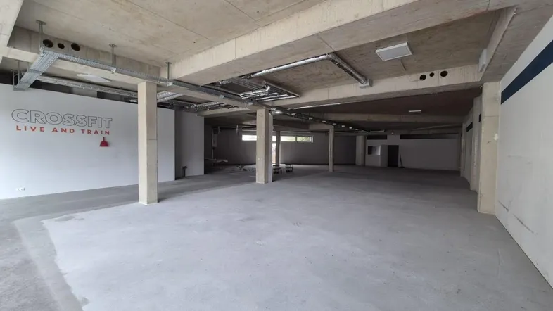 Großer, leerer Gewerberaum mit Betonboden und -decke, ideal für Fitnessstudios oder Lagerflächen.