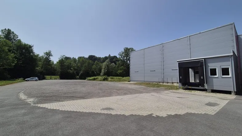 Außenansicht eines modernen Industriegebäudes mit Laderampe, großem Vorplatz und umgebender Natur.