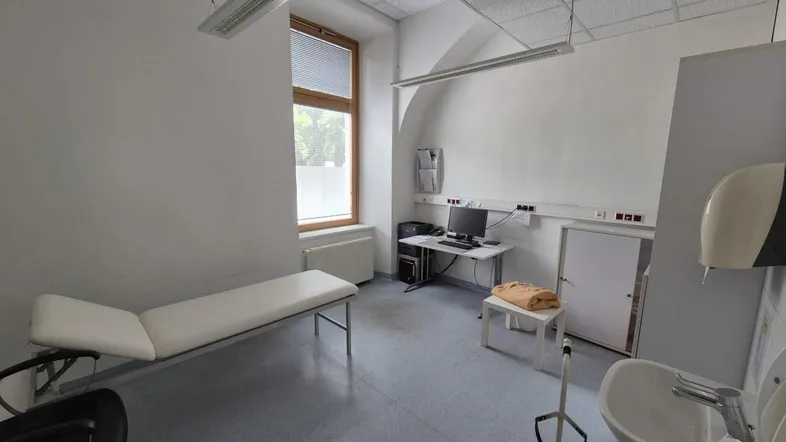 Heller Untersuchungsraum mit Liege, Schreibtisch und Waschbecken, ideal für eine Arztpraxis.