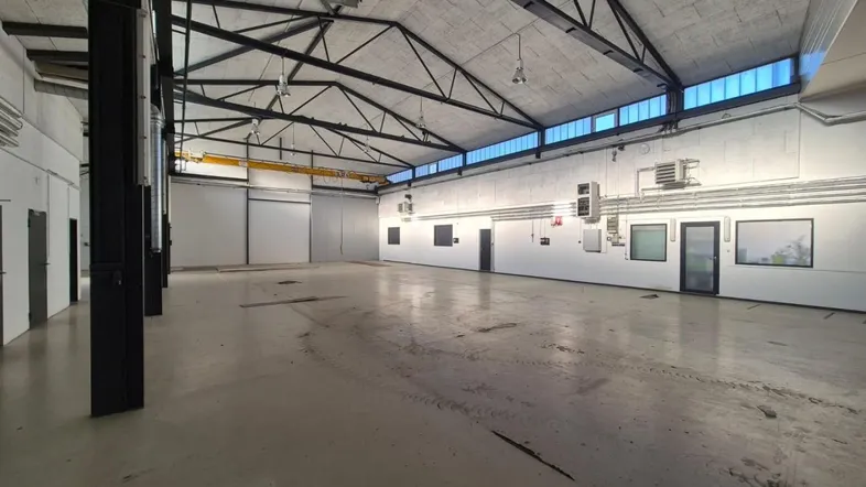Geräumige Lagerhalle mit hoher Decke, sichtbaren Stahlträgern und großen Oberlichtern für viel Tageslicht.
