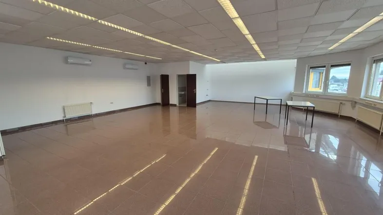 Geräumiger, leerer Büroraum mit Fliesenboden, abgehängter Decke und großen Fenstern für viel Tageslicht.
