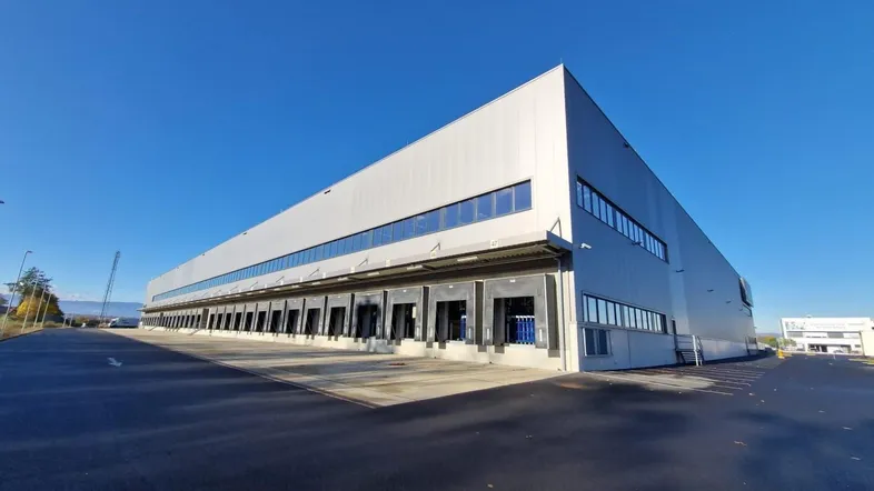 Großes modernes Industriegebäude mit zahlreichen Laderampen unter klarem blauem Himmel und weitläufigem Vorplatz.