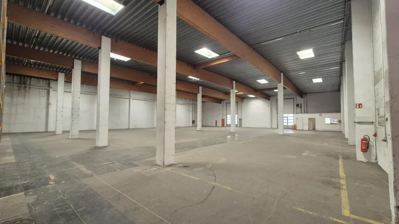 Geräumige Lagerhalle mit hohen Decken, sichtbaren Holzbalken und Oberlichtern für natürliches Licht.