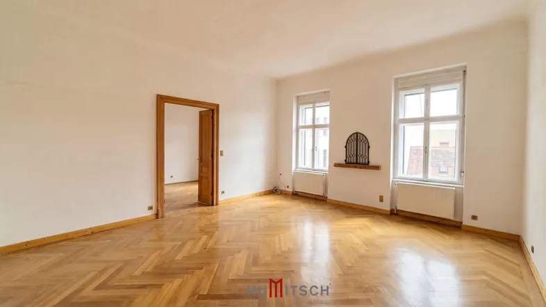 Helles Zimmer mit klassischem Fischgrätparkettboden, weißen Wänden und hohen Fenstern.