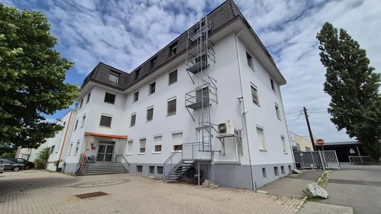 Weißes Geschäftsgebäude mit Mansarddach, externer Fluchttreppe und Klimaanlage an der Fassade.