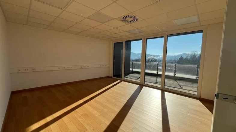 Heller Büroraum mit Holzboden, großen Fenstern und Bergblick, ideal für produktives Arbeiten.