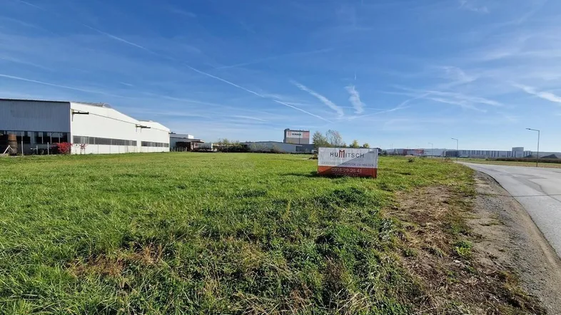 Weitläufiges Grundstück mit grüner Wiese und Blick auf Industriegebäude unter blauem Himmel.