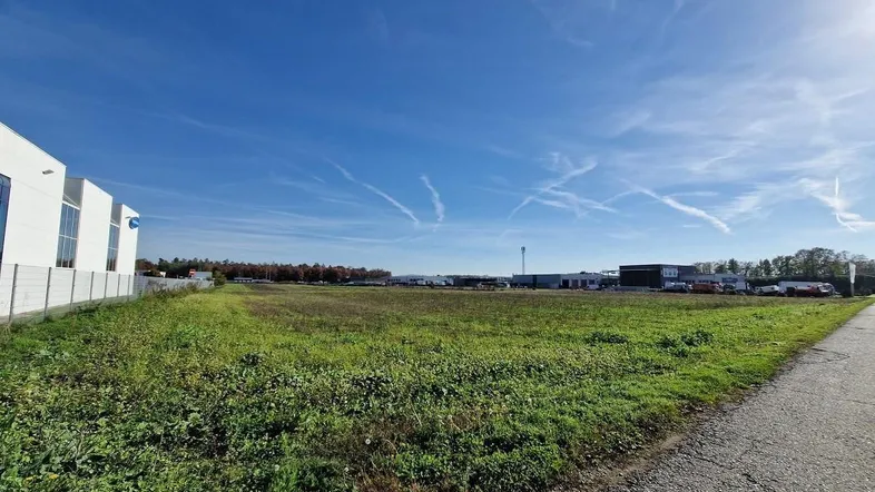 Weitläufiges Grundstück mit grüner Wiese und Blick auf umliegende Gewerbegebäude unter blauem Himmel.