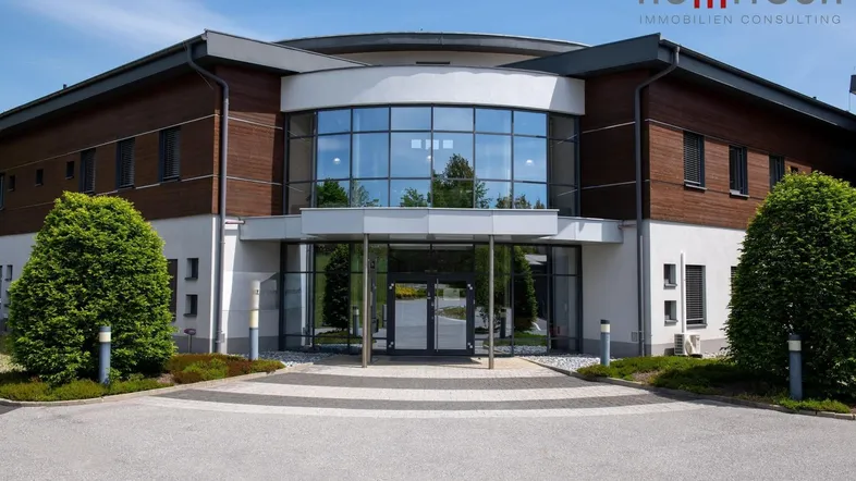 Modernes Bürogebäude mit großer Glasfassade und gepflegter Zufahrt unter blauem Himmel.