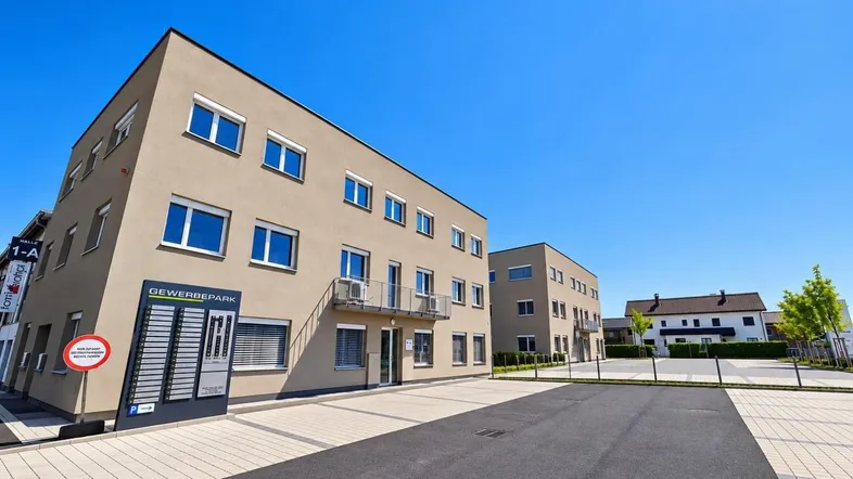 Modernes Gewerbegebäude mit beiger Fassade, blauen Fenstern und ausreichend Parkplätzen im Freien.