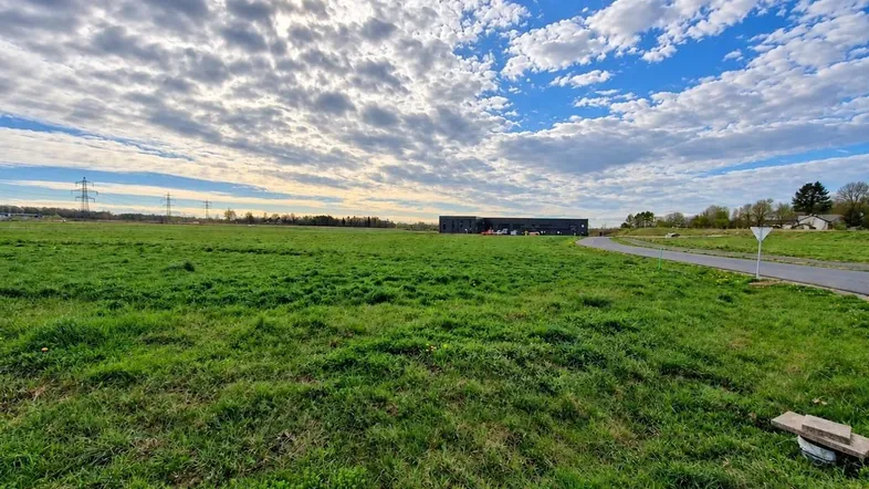 Weite grüne Wiese unter einem bewölkten Himmel mit einem Gebäude in der Ferne und Stromleitungen.